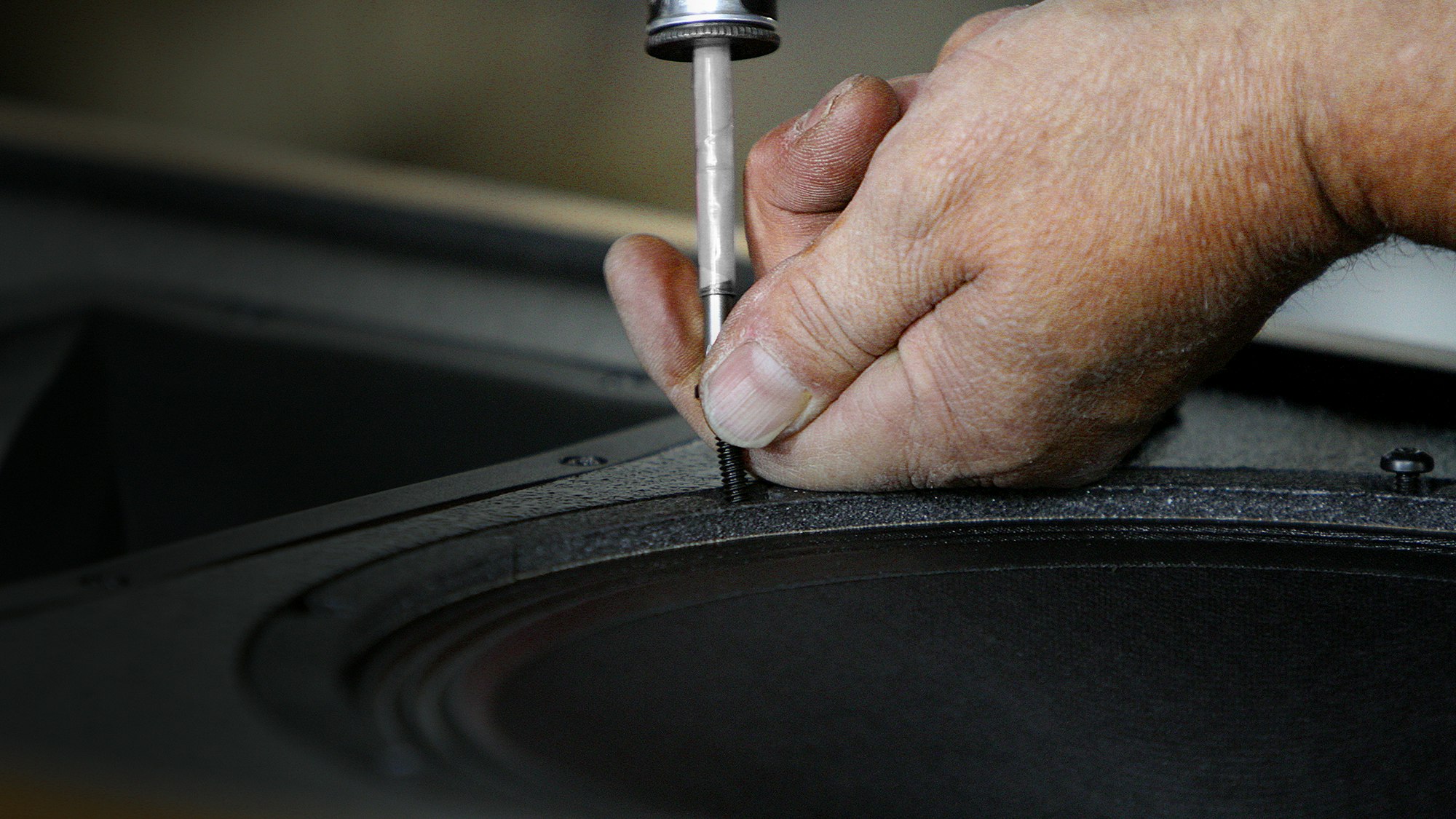 A Klipsch Craftsman hand fastening a speaker to its cabinet